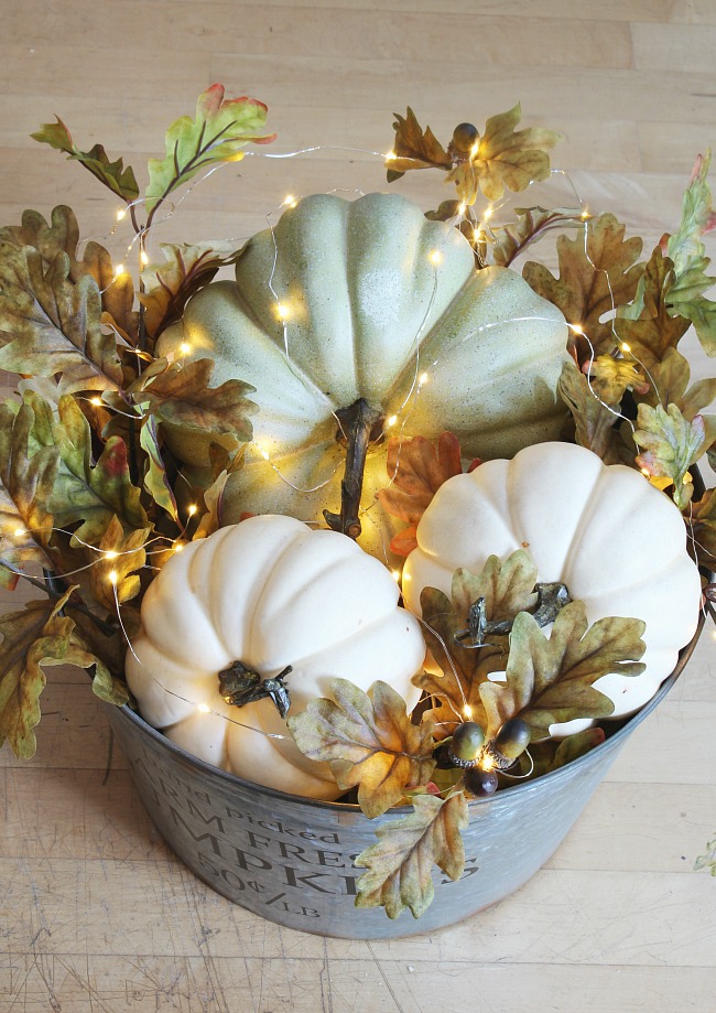 DIY lighted pumpkin basket. Galvanized metal bucket filled with pumpkins, fall leaves, and mini lights.