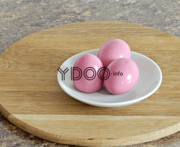 куриные яйца розового цвета лежат на блюдце на деревянной доске